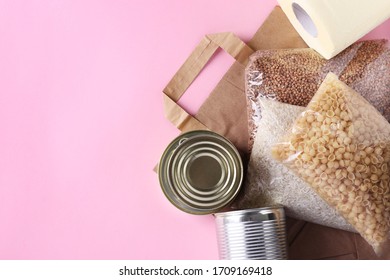 Paper bag with food supplies crisis food stock for quarantine isolation period on pink background. Rice, buckwheat, pasta, canned food, toilet paper. Food delivery, Donation, Copy space, Closeup - Shutterstock ID 1709169418