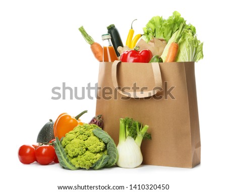 Paper bag with fresh vegetables and bottle of juice on white background