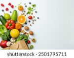 A paper bag full of fruits, vegetables and nuts on a white background with space for a text banner. The top view, flat lay shows healthy eating or shopping in a grocery store