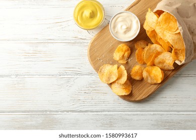 Paper bag of potato chips. Beer snacks, sauce on cutting board, on white wooden background, space for text. Top view - Powered by Shutterstock