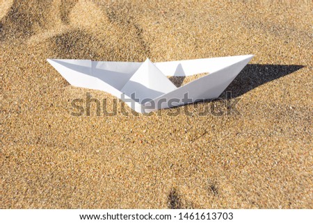 Paper boat buried in the sand on the beach, shipwreck concept, origami paper