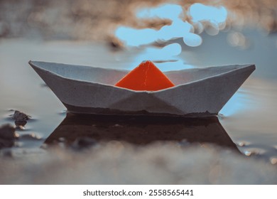 Paper Boat with Orange Sail Reflecting in Water, Symbolizing Minimalist Creativity and Childhood Nostalgia - Powered by Shutterstock