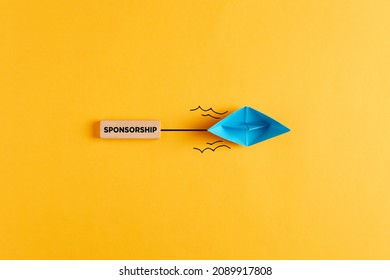 Paper boat pulls a wooden banner with the word sponsorship. Sponsoring, financial support or fundraising concept.