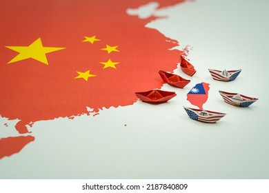 Paper boats with the colors of the USA and China surrounding the island of taiwan on a map
