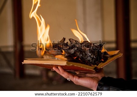 Paper book burns to ashes on concrete tiles, manuscript burns, open book with burning fire in man hand
