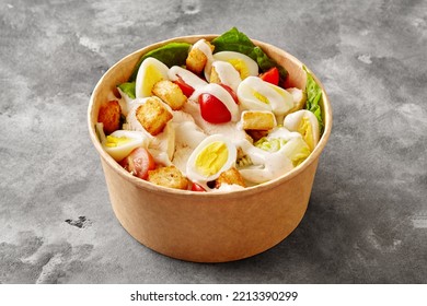 Paper Bowl Of Caesar Salad With Romaine Lettuce, Tomatoes, Quail Egg, Croutons, Chicken Fillet And Sauce