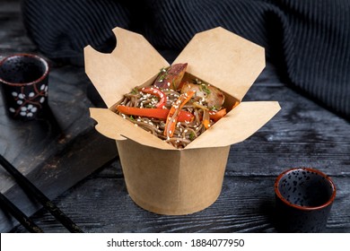 paper box with buckwheat noodle wok and grilled chicken fillet. decor on a black background.