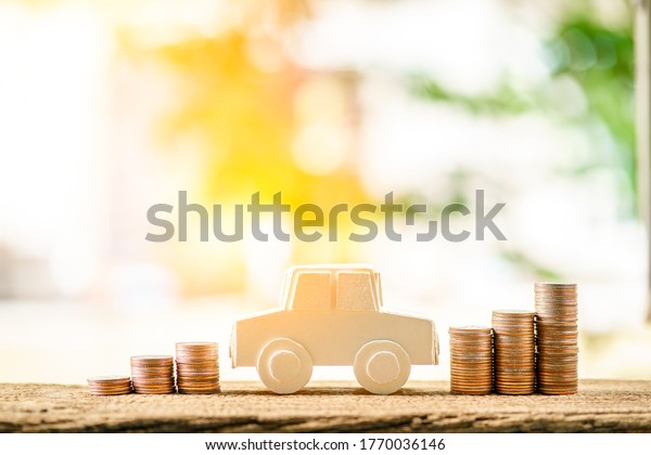 Paper car\
model and stacked gold coin with growing interest on sunlight in\
the public park, Saving money for buy a new chattel or loan\
business investment in the future\
concept.
