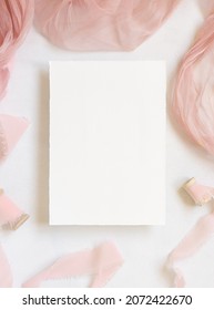 Papierkarte auf weißem Marmortisch mit getrockneten rosafarbenen Blumen und Seidenbändern Draufsicht. Flat lay mit vertikaler Blindkarte. Romantische Einladung oder Grußkartenmuster, Kopienraum