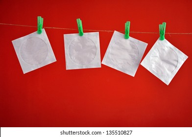 Paper CD Envelopes Hanging Clipped On The Rope In Front Of A Red Background