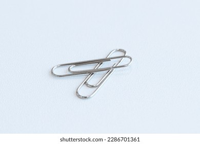 Paper clip on floor white background. Is device used to collect small number of documents together temporarily by inserting without damaging paper or document. Wire plated with nickel, and not rust.