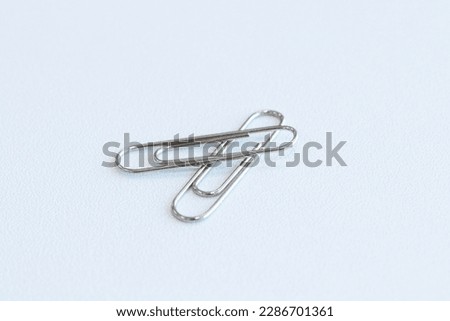 Paper clip on floor white background. Is device used to collect small number of documents together temporarily by inserting without damaging paper or document. Wire plated with nickel, and not rust.
