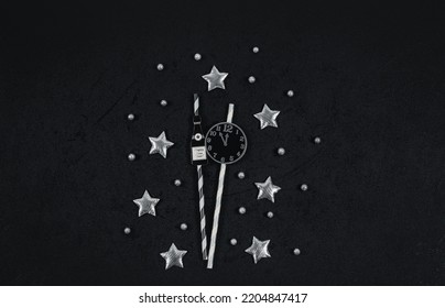 Paper Clock, Bottle Of Champagne On Straws, Silvery Stars And Snow Ball On A Black Background, Top View Close-up.New Year Celebration Concept.