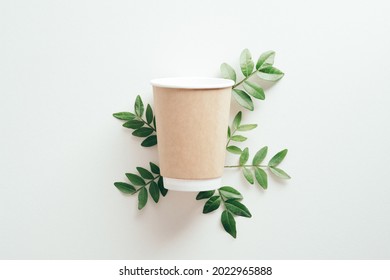 Paper Container Cup Of Coffee To Go With Green Leaves On White Background. Flat Lay, Top View.