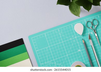 Paper crafting work table: scissors, craft knife, pencil, tweezers, eraser, paper on gray background. Space for your text.