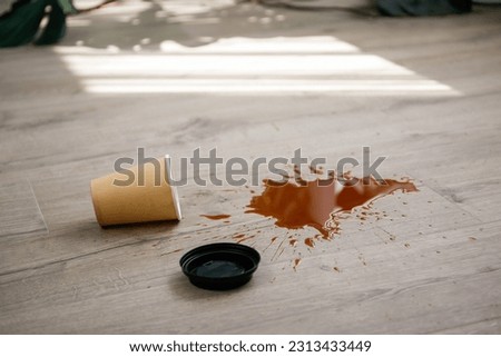 Paper cup of coffee fell on laminate, coffee spilled on floor.