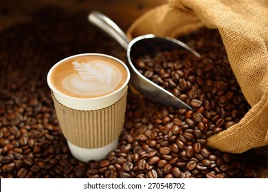 Paper cup of coffee latte and coffee beans on wooden table
