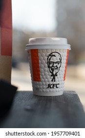 Paper cup from KFC restaurant with image of Colonel Sanders standing on bench outside, close-up. Background blurred, bokeh. Smolensk, Russia 04.12.2021