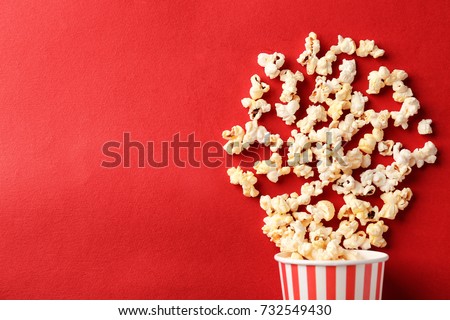 Paper cup with popcorn on color background