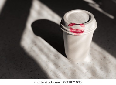 Paper cup with red lipstick kiss print on the table. Pink woman lips marks.