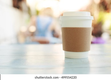 Paper Cup Of Takeaway Coffee On The Wooden Table In Cafe. Place For Your Text Or Logo.