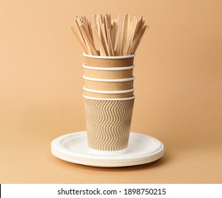 paper cup, white plates and wooden forks and knives on a brown background. Plastic rejection concept, zero waste 
