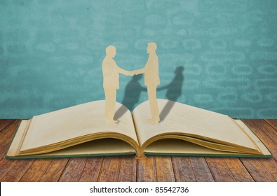 Paper Cut Of Two Business Man Shake Hand On Old Book