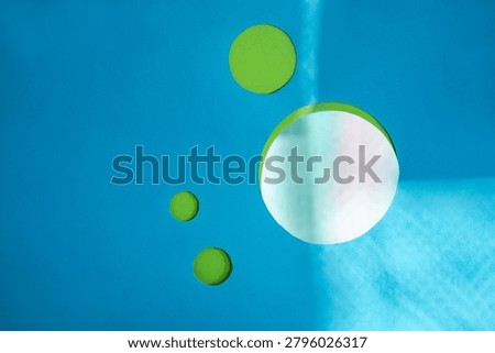 Paper cutout elements create tactile, handcrafted quality within minimalist geometric composition. Paper cut green circles with mirror disc on turquoise blue background.