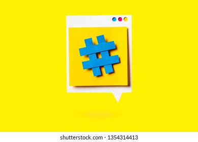 Paper cutout of hashtag symbol on a yellow speech bubble on yellow background. Concept of social media and digital marketing.