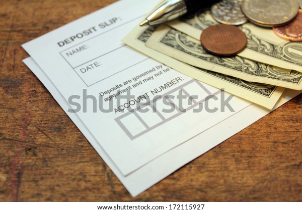paper deposit slip, spare change and pen over\
wood background