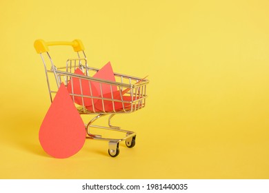 Paper Drops Of Blood And Shopping Trolley On Yellow Background, World Donor Day Concept, Donate Blood For Money, Donor Blood Bank