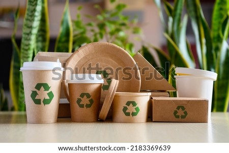 Paper eco-friendly disposable tableware with recycling signs on the background of green plants. The concept of using biodegradable materials.