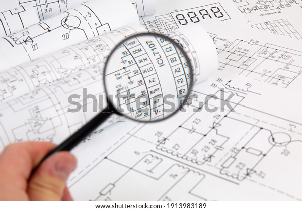 Paper electrical engineering\
drawings and magnifying glass. Work of an electronic\
engineer.