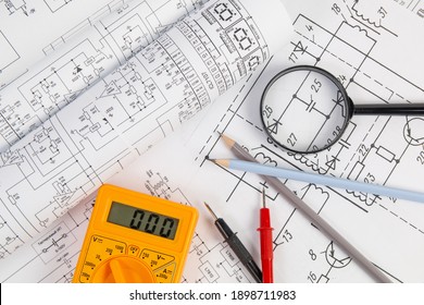 paper electrical engineering drawings, pencil, magnifying glass and digital multimeter