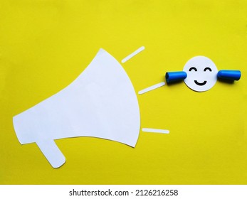 A paper face with earplugs protects against the sounds of a loudspeaker. Noise protection, application on a yellow background - Shutterstock ID 2126216258