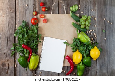 Paper Grocery Bag With Blank Notebook And Fresh Vegetables And Fruits On Wooden Table Top View. Eco Shopping Concept And Product List For Cooking