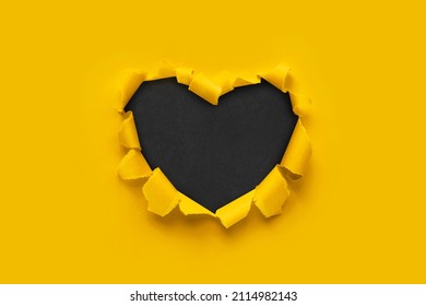 A paper hole with torn edges on a yellow background. Through paper. A ragged hole in the shape of a heart. Valentine's day. A symbol of love, romantic relationships. International Women's Day.