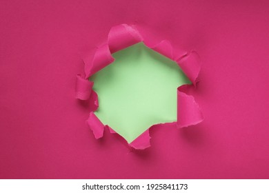 Paper hole with torn sides on a crimson, pink background. Through the paper. A ragged hole.An accurate shot. The concept of advertising and breakthrough. Design for text, print, or advertising content
