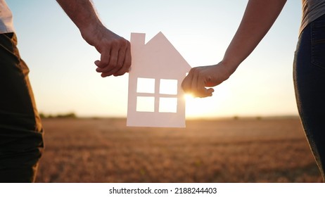 Paper House Happy Family. Friendly Family Hands Holding Paper House The Glare Of The Sun Shine Through The Window A Beautiful Sunset. Mortgage Business Construction Concept. House Dreams Lifestyle