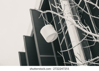 A paper lantern hangs from bare tree branches against a modernist building backdrop. Stark monochrome highlights geometric patterns in this minimalist urban scene, emphasizing texture with high-contrast lighting.