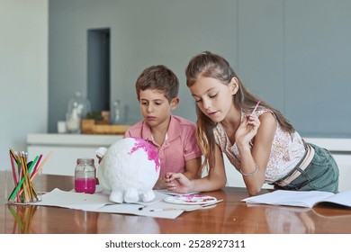 Paper mache, painting and kids at table together for growth, creative development or homeschool for sibling bonding. Art, craft and children drawing with watercolor, brush and fun project in home - Powered by Shutterstock