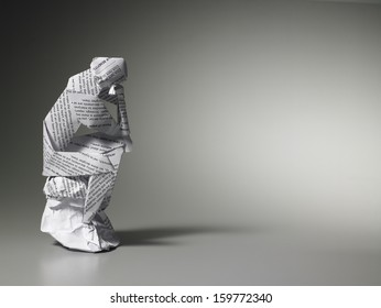 Paper man deep in thought sitting on rock