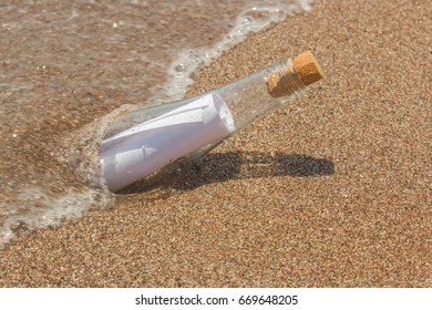 Paper Message in a glass bottle with a cork on the sand. In the background, the sea and waves. A note on salvation, please help - Shutterstock ID 669648205