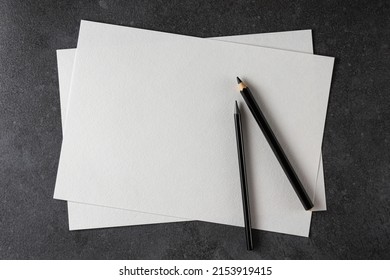 Paper mockup. Watercolor A4 paper with black pencils on dark background. Top view. Can be used as a template for drawings. - Shutterstock ID 2153919415
