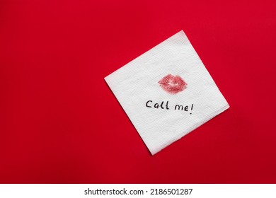 Paper napkin with lipstick mark and words CALL ME on red background, top view. Space for text