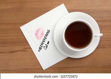 Paper Napkin With Phone Number And Lipstick Mark Under Tea Cup On Wooden Table, Top View