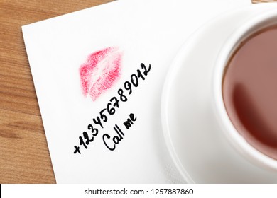 Paper Napkin With Phone Number And Lipstick Mark Under Tea Cup On Wooden Table, Top View