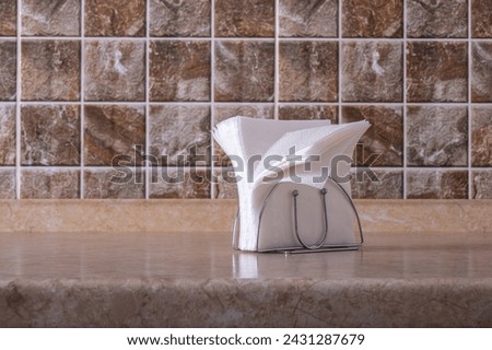 Paper napkins in chrome holder on the table against the background of a tiled wall.
