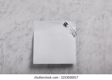 Paper note with safety pin on grey textured background, top view