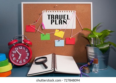 Paper Note Written With TRAVEL PLAN Inscription On Cork Board. Eye Glasses, Alarm Clock, Plant And Books On Wooden Desk.Artificial Grain Effect.